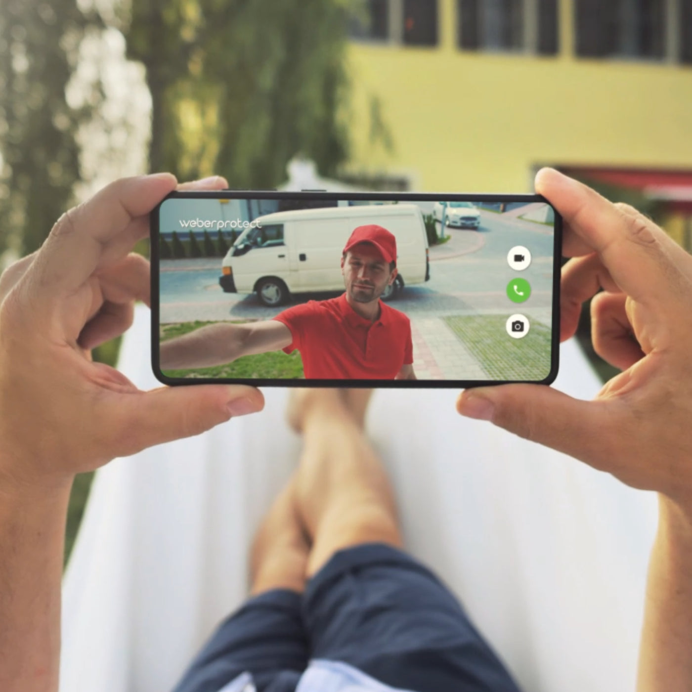 Mann hältSmartphone mit Live Feed der Postbote an der Eingangstür zeigt